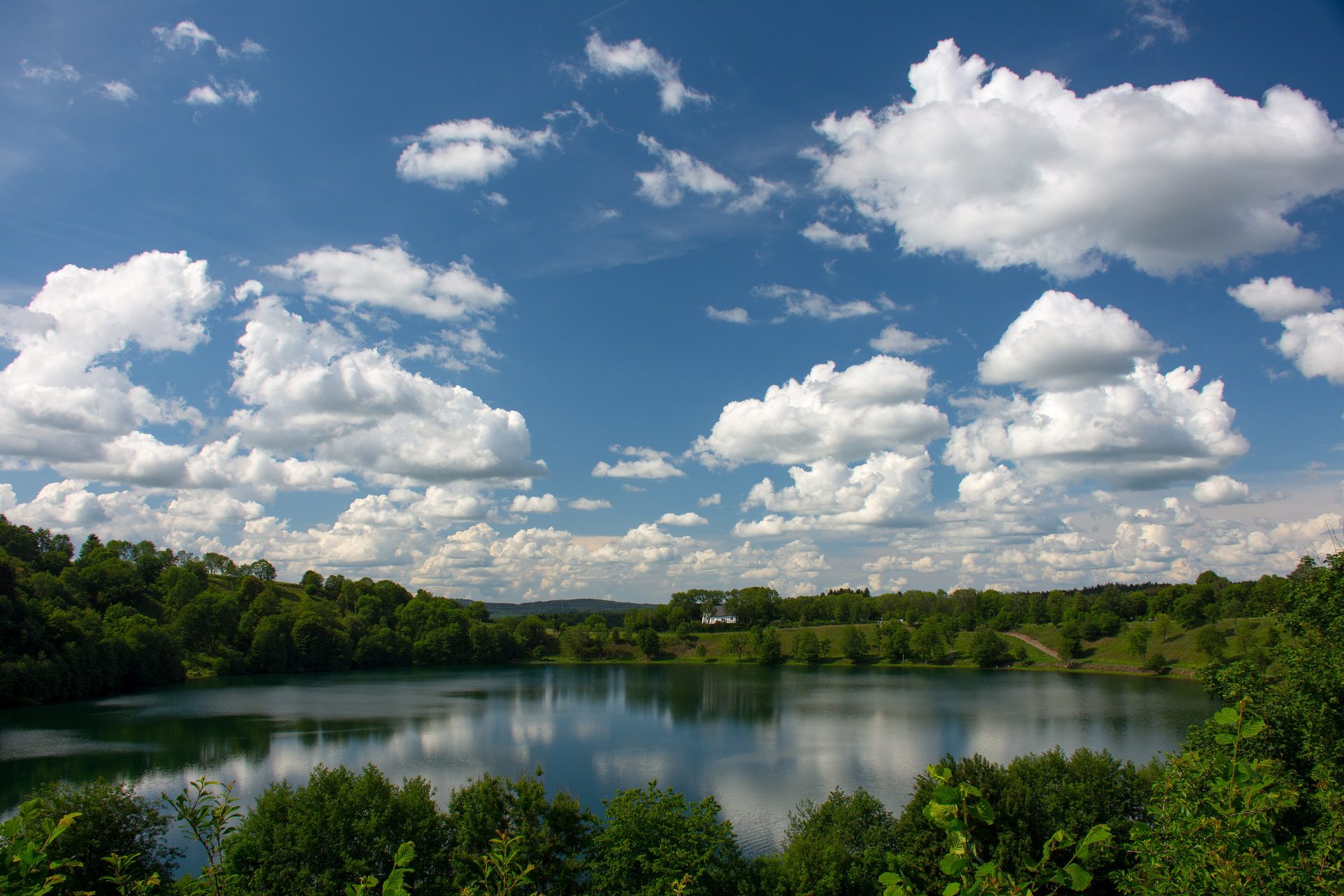 Eifelsteig am Weinfelder Maar: Blick über den Maarsee in der Vulkaneifel, Quellwolken spiegeln sich im Wasser